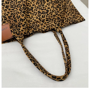 Close-up of leopard print canvas tote bag with a brown leather logo tag and fabric strap