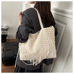 Detail of white crochet tote bag with long fringe tassels shown on model's shoulder