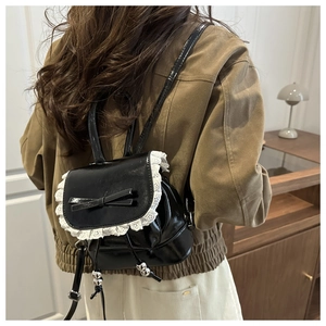 Detail of black glossy mini backpack with white lace trim and bow on model