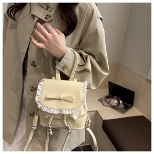 Detail of cream mini backpack with lace trim and bow accent shown in a cafe setting