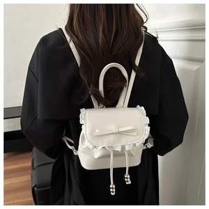 Detail of white mini backpack featuring lace edges, a bow, and metal bead drawstrings