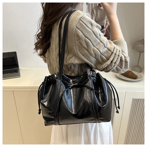 Detail view of a black glossy patent leather shoulder bag with an elegant ribbon bow design
