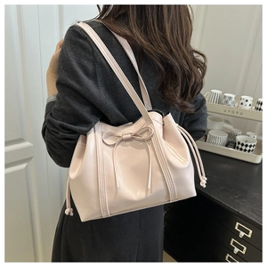 Detail of a large pink glossy PU tote bag with a bow accent worn as a shoulder bag