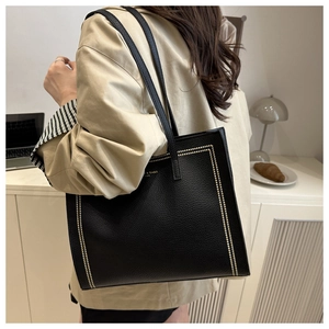 Close-up of black leather tote bag with gold rivet details on shoulder strap