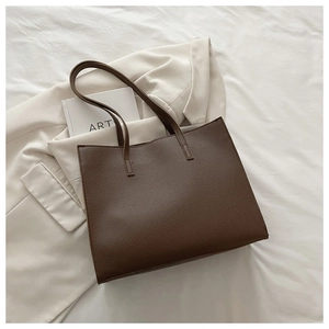 Detailed close-up of brown litchi-grain leather tote bag on minimalist white fabric