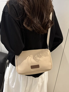 Minimalist beige crossbody bag with brown leather patch shown on model back