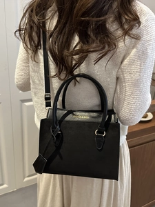 Sac à main noir élégant avec détails dorés et bandoulière porté par un mannequin