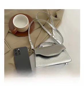 Detailed close-up of silver metallic clutch bag showing texture and size with a phone