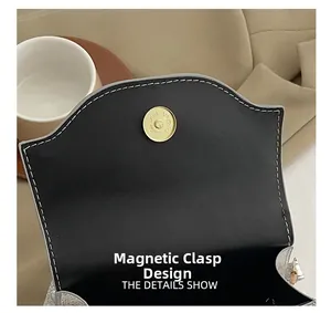 Detail of premium golden magnetic closure on black leather evening bag with white stitching
