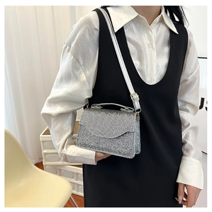 Silver sequin evening bag with top handle and chain strap worn over a white shirt