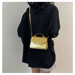 Golden wave-pattern evening bag styled as a crossbody on a model in a black outfit
