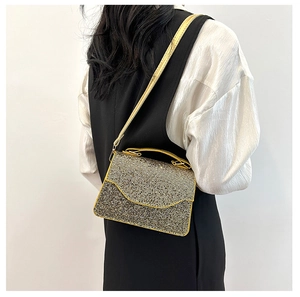 Detailed view of a gold rhinestone clutch bag with a metallic chain on a model