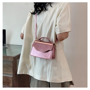 Back view of model wearing a pink metallic clutch bag with chain strap and top handle