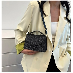 Close-up of glitter fabric handbag with top handle and leather strap on model