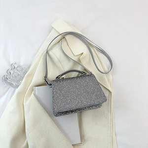 Detail of silver sparkling evening bag with chain strap on a white blazer background