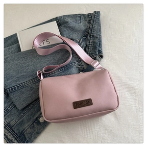 Détail du sac bandoulière en nylon rose clair avec étiquette en cuir sur fond denim