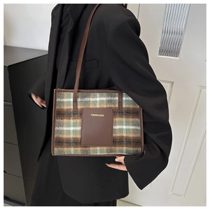 Detail of green plaid tote bag with faux leather strap and fashion label on tweed