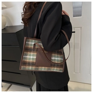 Plaid tote bag in green and brown wool with leather straps shown from a side view on a model