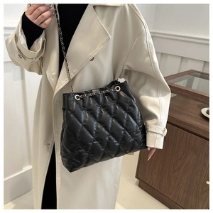 Detail of black quilted bucket bag with gold chain strap worn by a model in interior setting