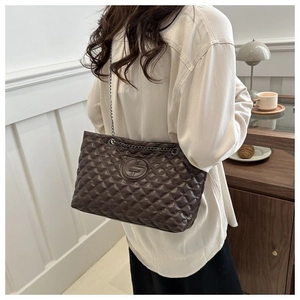 Detail of coffee brown quilted chain bag worn over shoulder in elegant indoor setting