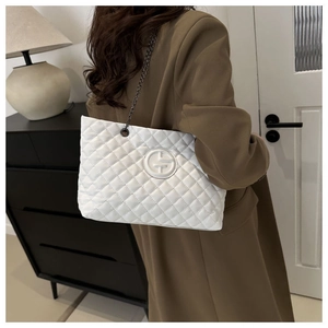 Detail of white quilted tote bag featuring a round logo and metal chain shoulder strap