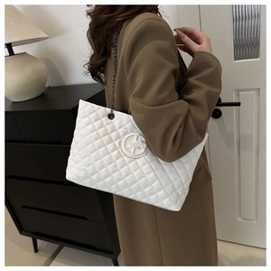 Detail of white quilted tote bag with chain strap shown on model in a modern room