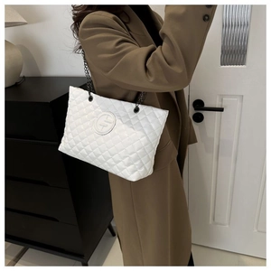 Detail of white quilted tote bag featuring metal chain strap and embossed logo