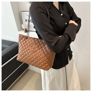 Detail of brown quilted tote bag with metallic chain strap and embossed logo texture