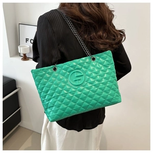 Detail of green quilted tote bag with chain strap and embossed logo on faux leather