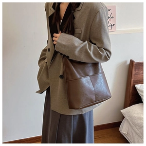 Detail view of large brown leather tote bag with front pockets on minimal home background