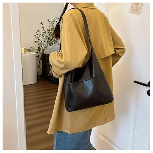 Detail of glossy black large tote bag with vertical stitch pocket on beige trench coat