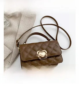 Close-up of quilted caramel leather handbag featuring a gold heart clasp on a suit blazer