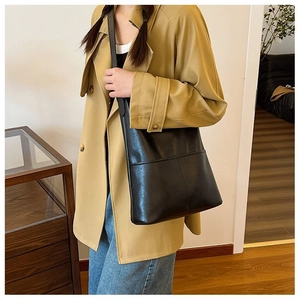 Detail of minimalist black leather tote bag showing exterior front pocket layers and texture