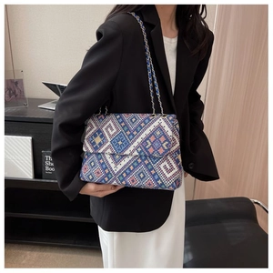 Detail of colorful geometric woven tapestry bag with metallic chain strap worn by a model