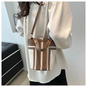 Detail of canvas and leather bucket bag showing contrast stitching and slim strap on model