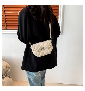 Détail d'un sac bandoulière matelassé beige avec fermoir porté par un mannequin