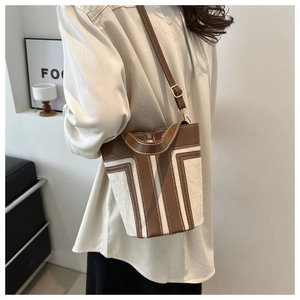 Detailed side view of bucket bag showing contrast stitching on beige canvas and brown leather