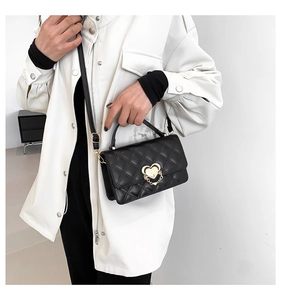 Detail of black quilted crossbody bag featuring a golden heart-shaped lock and chain strap