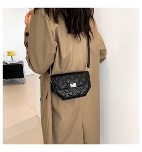Détail du sac bandoulière matelassé noir avec fermoir rotatif porté sur un trench-coat