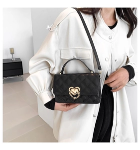 Close-up of black quilted crossbody bag with heart-shaped gold clasp and chain detail