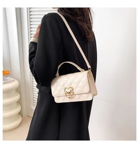 Detail of quilted diamond pattern and golden heart-shaped clasp on a cream leather bag