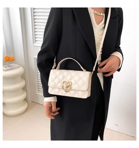 Detail of off-white quilted crossbody bag featuring a golden heart buckle on a black blazer