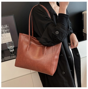 Dettaglio della borsa tote in pelle marrone caramello con texture fine su cappotto nero