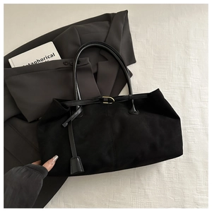 Close-up of black suede tote bag with fine stitching and gold buckle detail