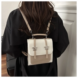 Détail d'un sac à dos chic crème et kaki avec boucle étoile porté sur un manteau noir