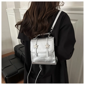 Mini sac à dos argenté avec boucles en étoile porté sur un manteau noir élégant