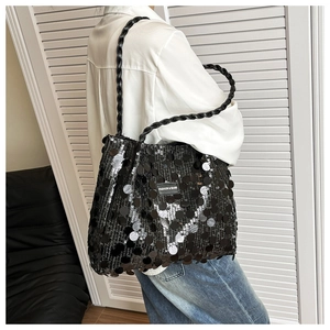 Detail of a black sequin tote bag with woven handles and a central fashion label