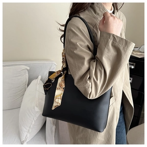Detail of black leather tote bag with white contrast stitching and a silk scarf handle wrap