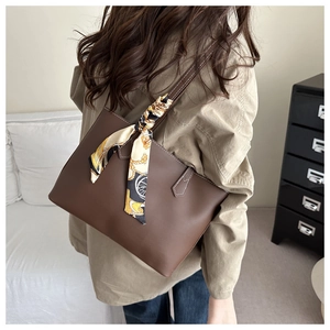 Detail of dark brown leather tote bag with white stitching and decorative silk scarf handle