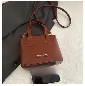 Detail view of mini brown crossbody bucket bag with metal 'FASHION' tag and top handle